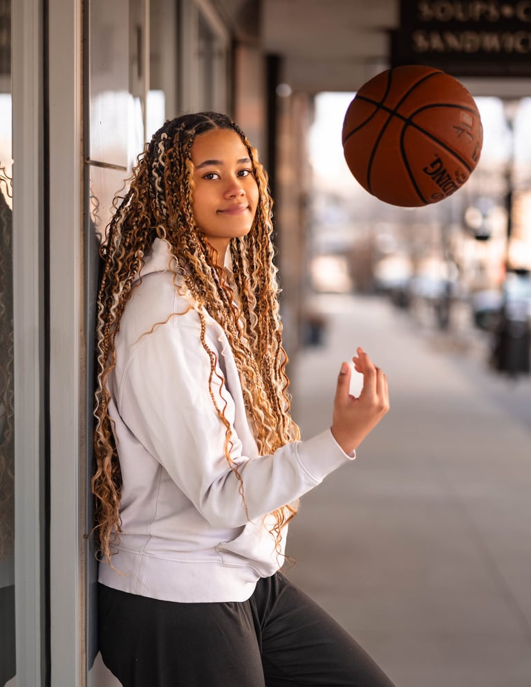 Young woman with braided hair in white hoodie spinning basketball with her finger on urban street
