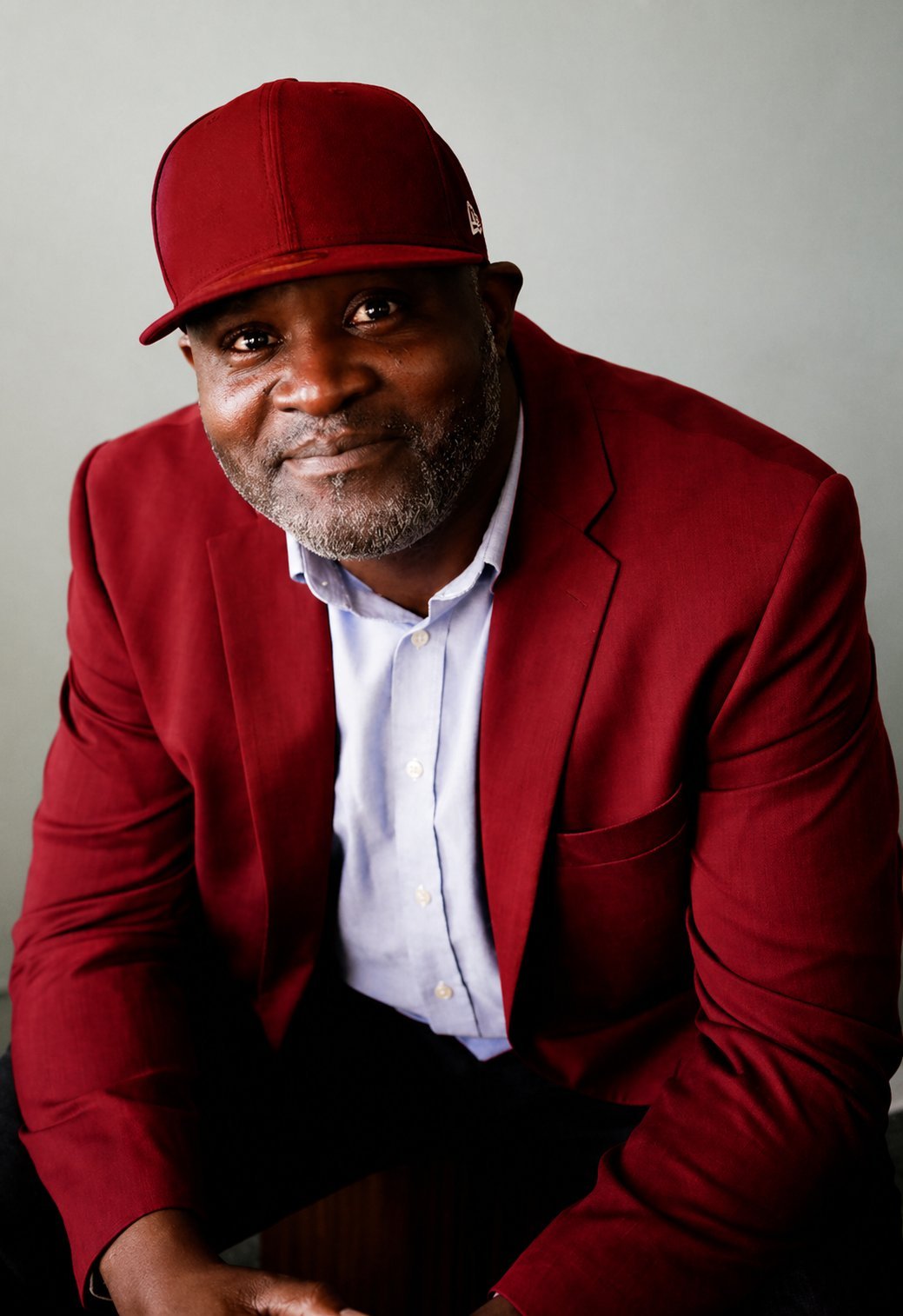 Man in red blazer and red baseball cap sitting with a friendly smile