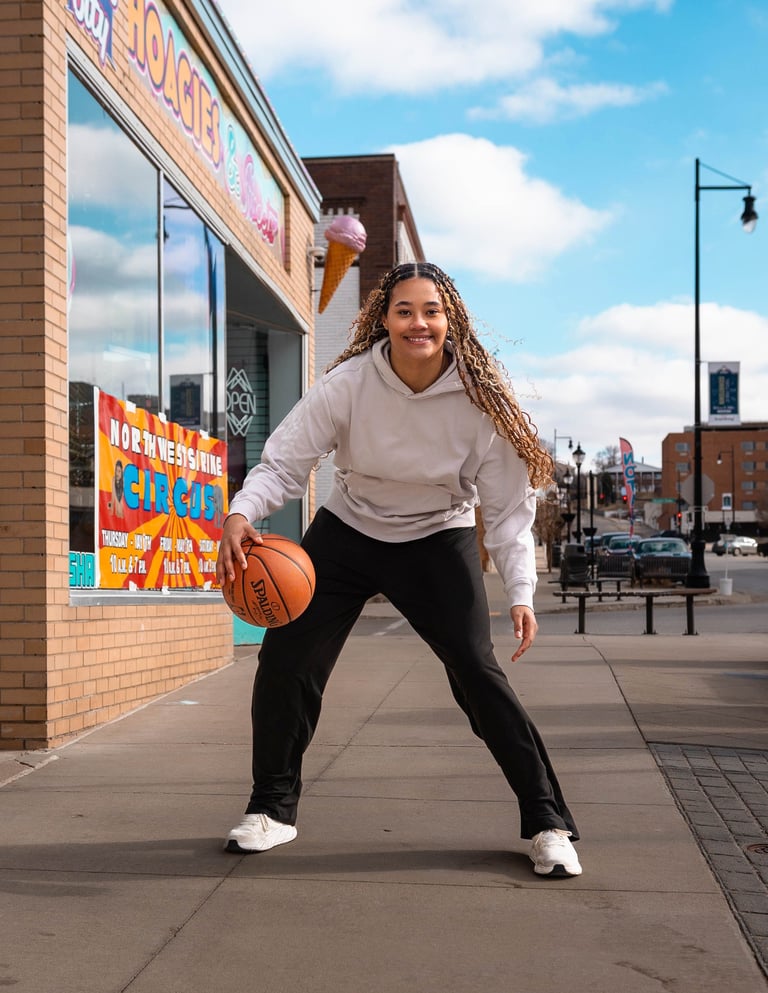 Young woman in athletic stance dribbling basketball on urban sidewalk